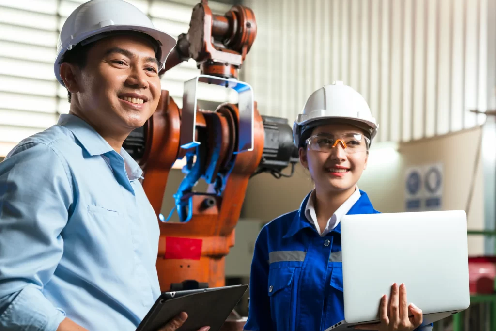 Male and female engineers collaborate together in manufacturing factory with their laptop and tablet